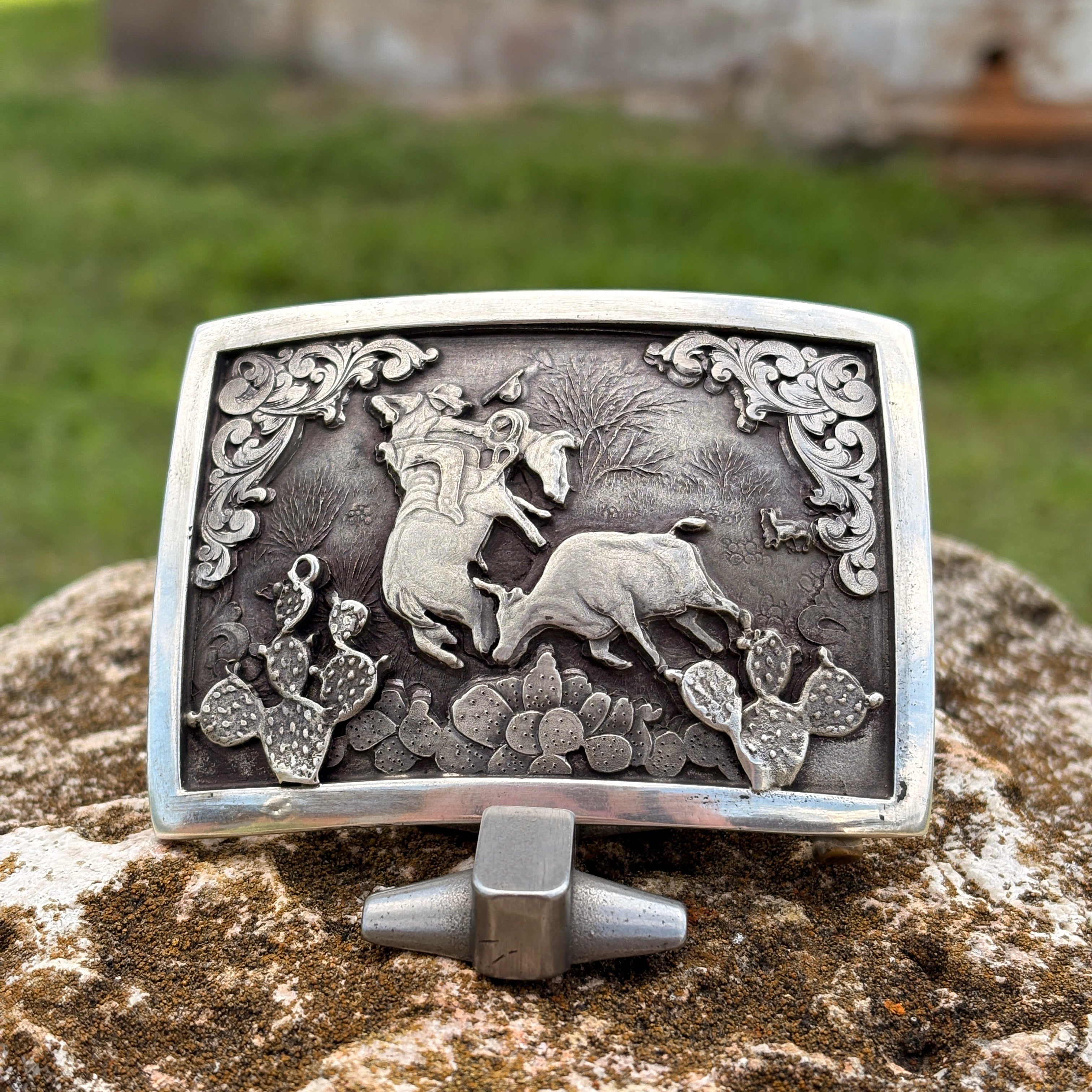 Silver belt buckle with intricate design of animals on a stone surface